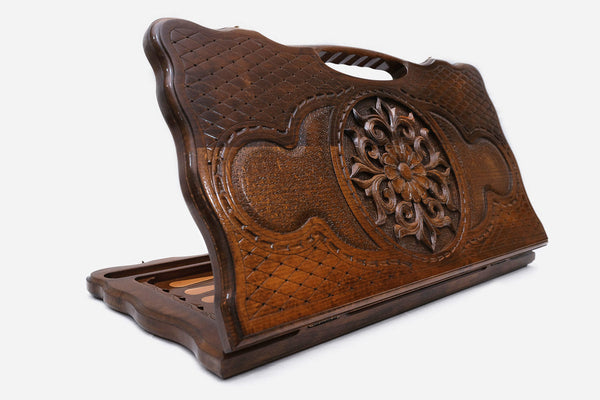 Carved beechwood backgammon board with a flowering carved ornament and a carry handle, propped open