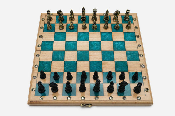 Folding chess board in pale wood with teal epoxy squares and ornate bronze figural pieces - gold and black armies in starting position