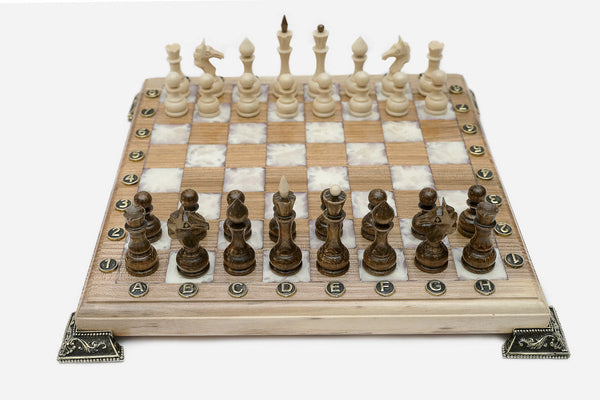 Chess board in pale wood with white marbled epoxy squares, brass corner brackets and wooden pieces set up for play