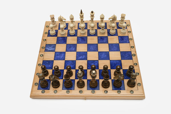 Compact folding chess board in pale wood with royal-blue epoxy squares and wooden pieces set up for play