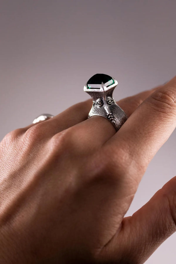 Close-up of a hand wearing a silver ring with a black gemstone on a neutral background