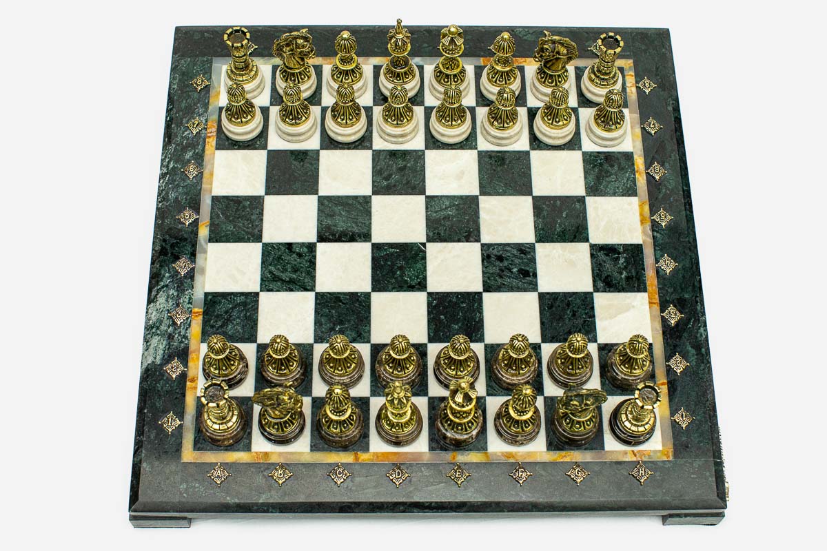 Angled overhead view of the green marble chess board with bronze pieces set up for play