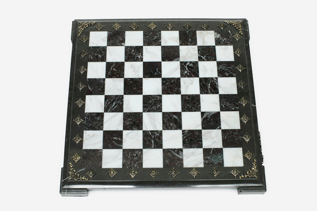 Top-down view of the empty burgundy and white marble chess board with a grey border and brass coordinate markers