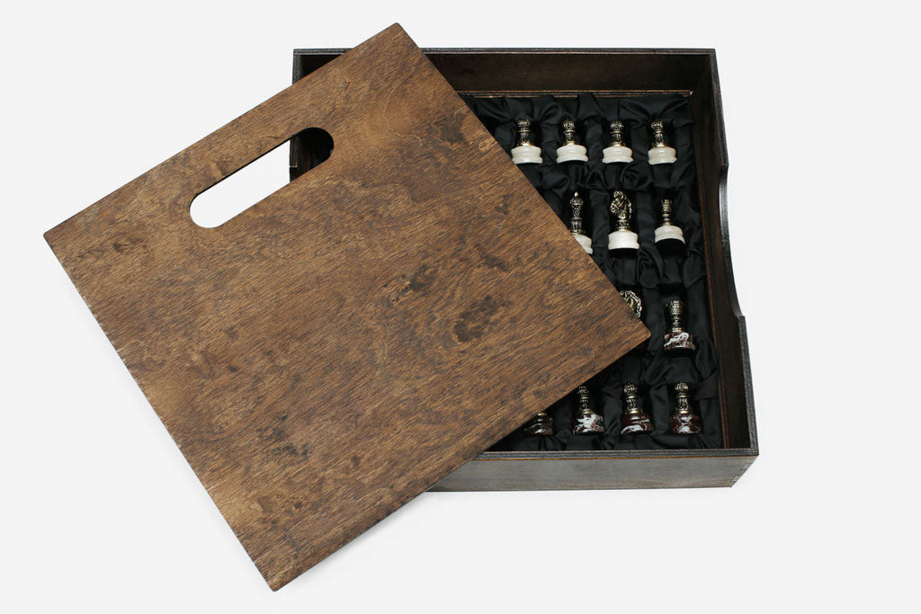 Wooden carry box with slot handle open beside the marble chess set, pieces resting in black satin