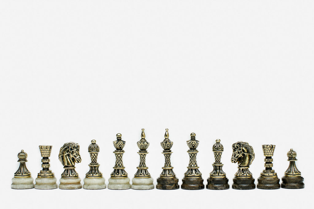 Row of the two-tone bronze chess pieces on marble bases, showing kings, queens, bishops and horse-head knights