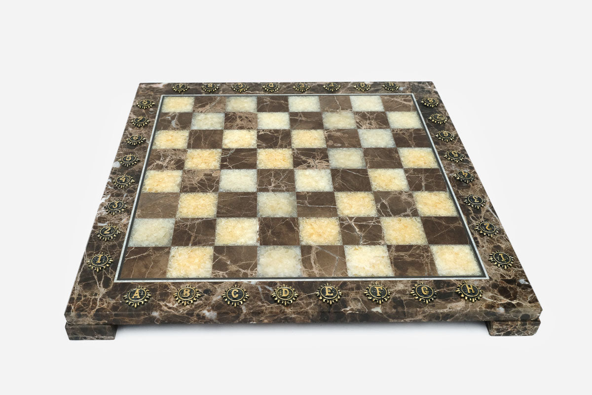 Elevated angle of the polished brown marble chessboard with its brass-studded border