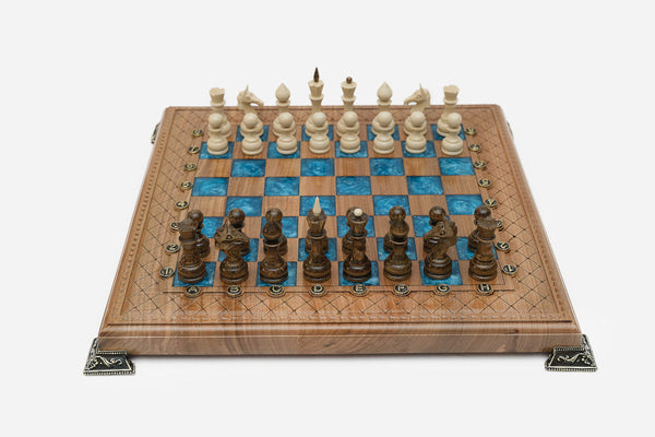 Chess board in walnut with blue epoxy squares, brass corners and wooden pieces set up for play