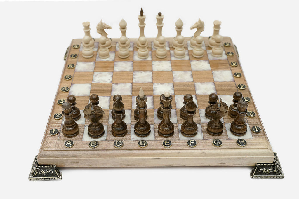 Chess board in pale wood with white marbled epoxy squares, brass corner brackets and wooden pieces set up for play