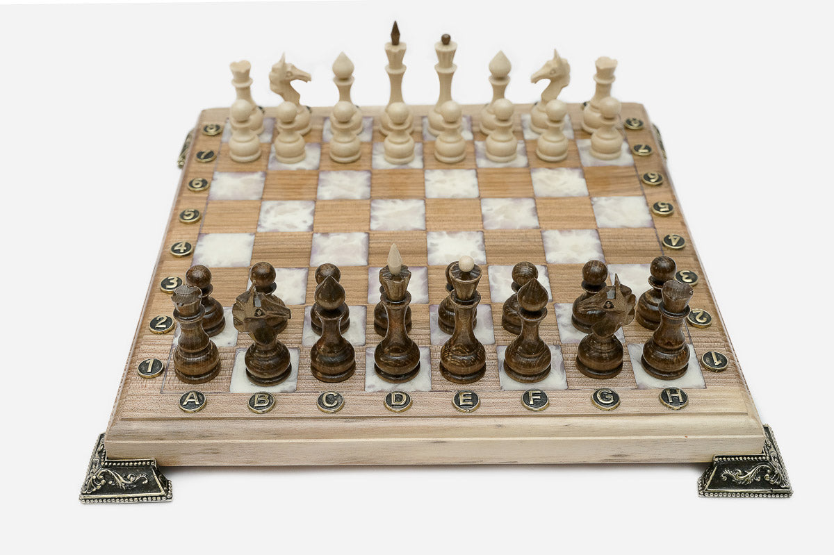 Chess board in pale wood with white marbled epoxy squares, brass corner brackets and wooden pieces set up for play