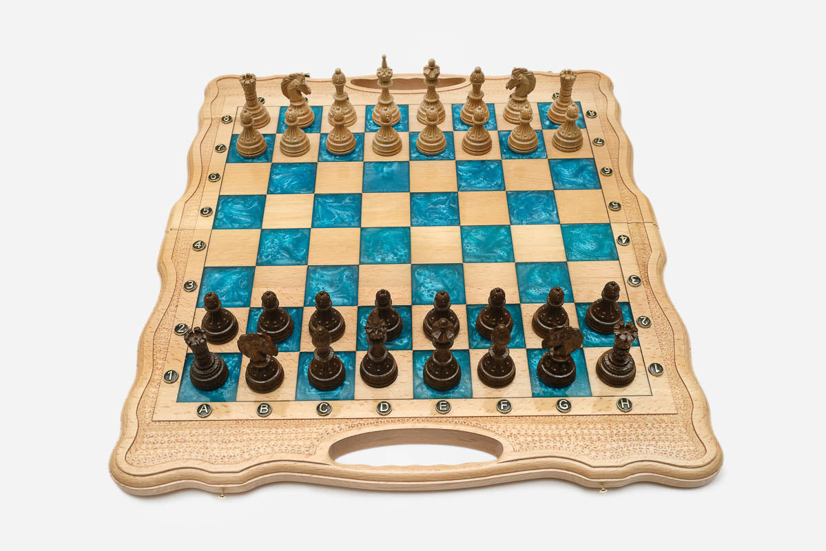 Folding chess board in pale wood with turquoise epoxy squares and ornately carved wooden pieces set up for play