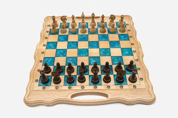 Folding chess board in pale wood with turquoise epoxy squares and ornately carved wooden pieces set up for play
