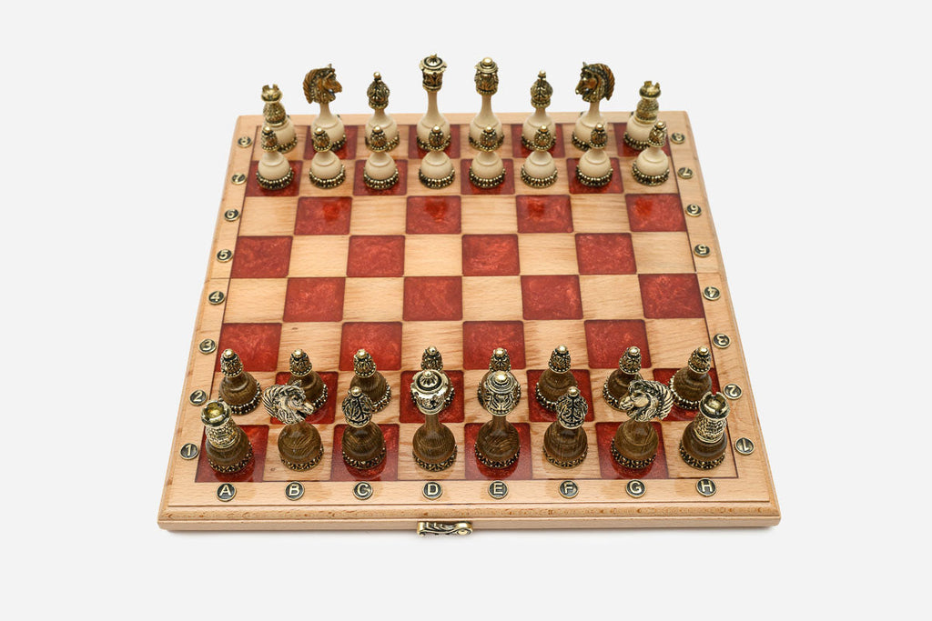 Folding chess board in pale wood with red epoxy squares and ornate bronze figural pieces set up for play