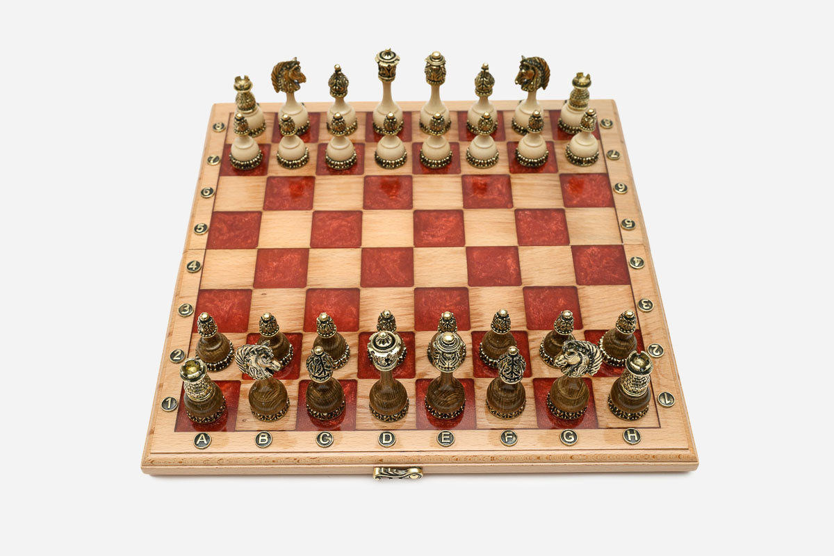 Folding chess board in pale wood with red epoxy squares and ornate bronze figural pieces set up for play