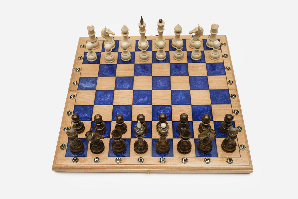 Compact folding chess board in pale wood with royal-blue epoxy squares and wooden pieces set up for play