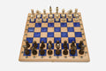 Compact folding chess board in pale wood with royal-blue epoxy squares and wooden pieces set up for play