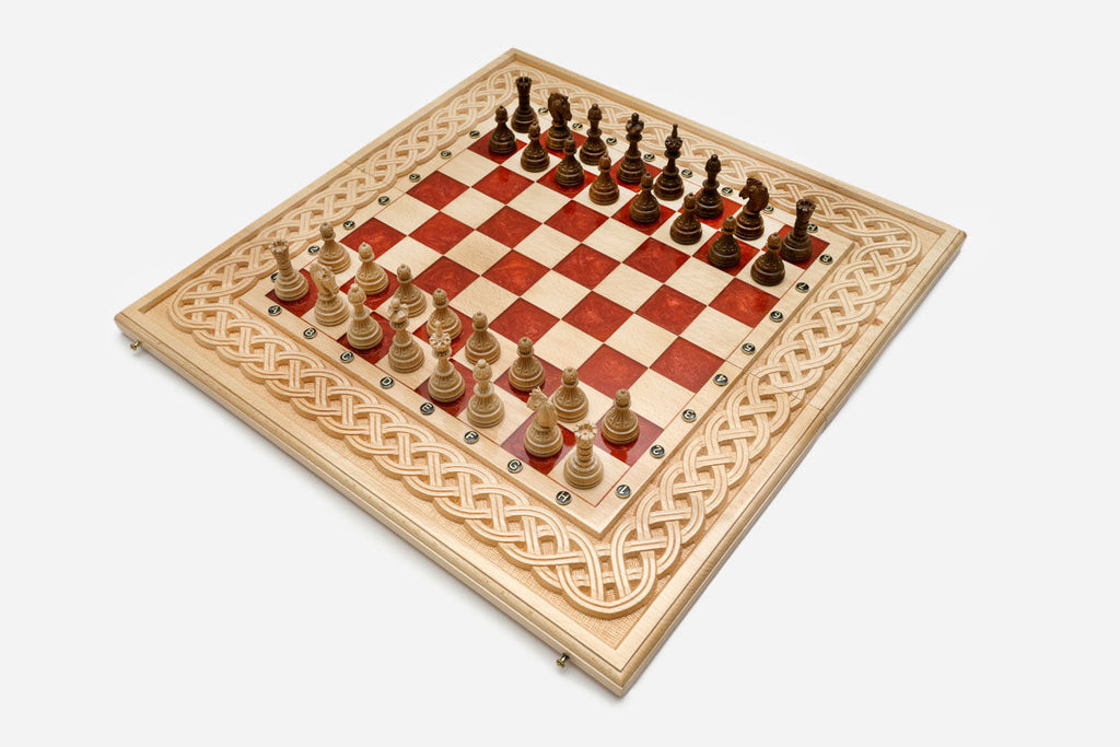 Large folding chess board in pale wood with red epoxy squares, a carved Celtic-knot border and wooden pieces set up for play