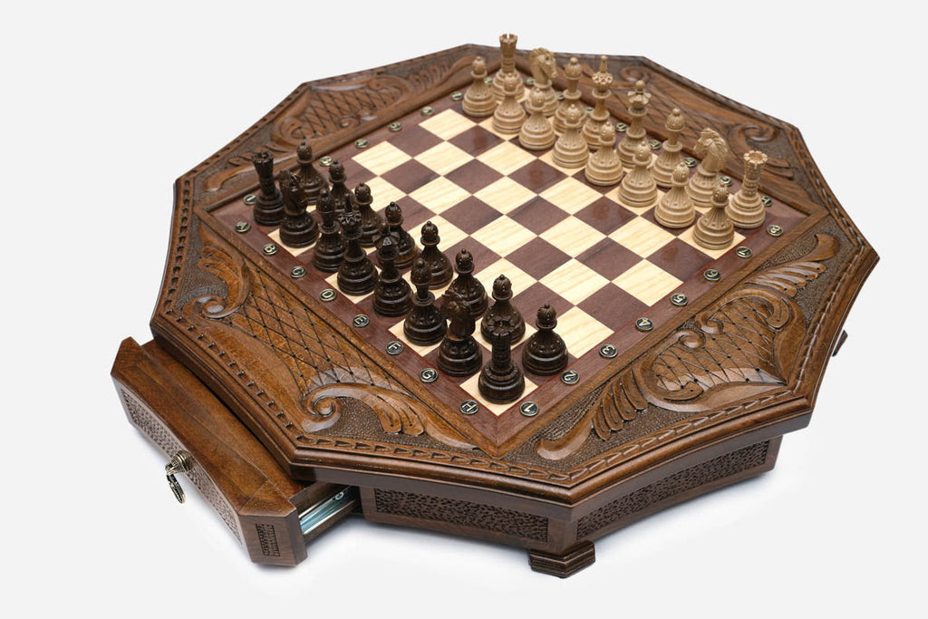 Angled view of the octagonal chess set with its storage drawer open and carved pieces on the board