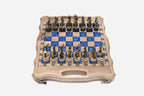 Compact folding chess board in pale wood with blue epoxy squares and figural bronze Greek-warrior pieces set up for play