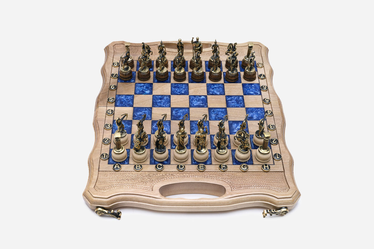 Compact folding chess board in pale wood with blue epoxy squares and figural bronze Greek-warrior pieces set up for play