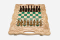 Folding chess board in pale wood with green epoxy squares, carved grape-vine borders and wooden pieces set up for play