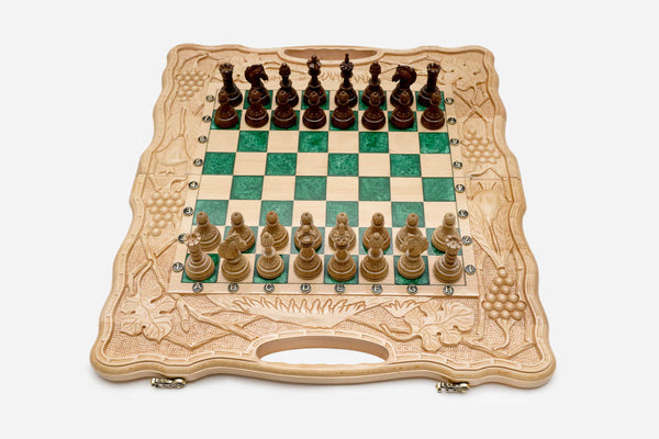 Folding chess board in pale wood with green epoxy squares, carved grape-vine borders and wooden pieces set up for play