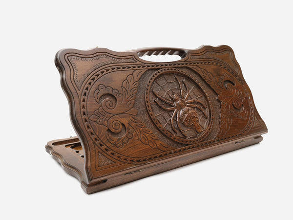 Hand-carved wooden backgammon board with a spider on its web and a cut-out carry handle, propped open