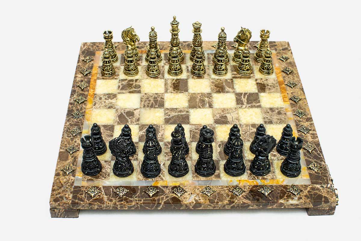Angled view of the marble and onyx chess board with gold and dark bronze pieces set up for play