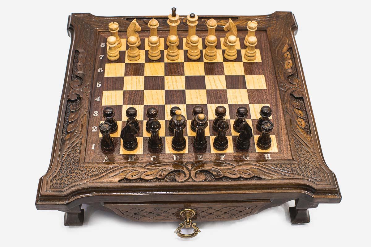 Compact dark walnut chess set with scroll-carved corners and wooden pieces set up on the inlaid board