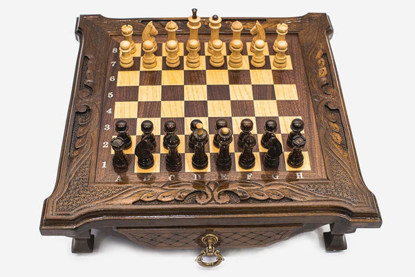 Compact dark walnut chess set with scroll-carved corners and wooden pieces set up on the inlaid board