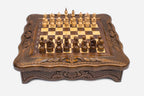 Compact carved wooden chess set with scalloped frame and wooden pieces set up on the honey-walnut board