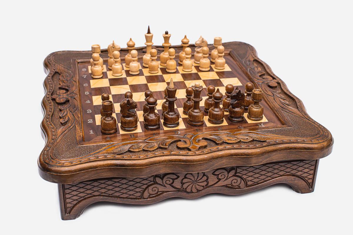 Angled view of the compact chess set with scalloped carved frame and pieces set up on the board