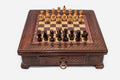 Compact wooden chess set with diamond-lattice carved border and wooden pieces set up on the inlaid board