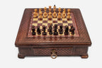 Compact wooden chess set with diamond-lattice carved border and wooden pieces set up on the inlaid board