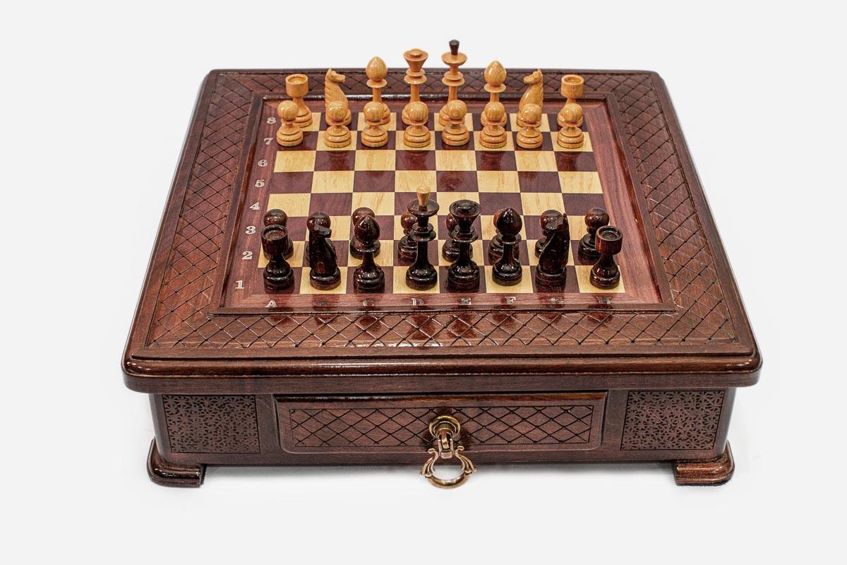 Compact wooden chess set with diamond-lattice carved border and wooden pieces set up on the inlaid board