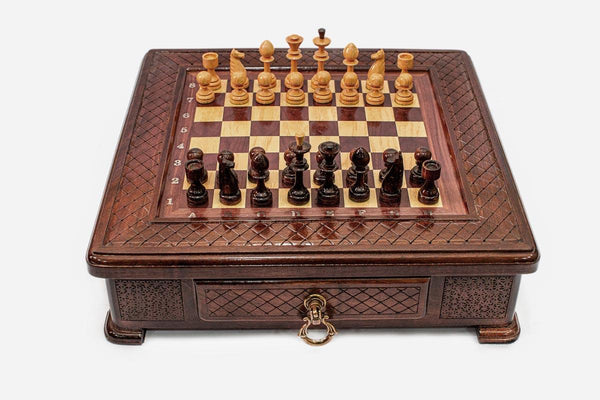Compact wooden chess set with diamond-lattice carved border and wooden pieces set up on the inlaid board