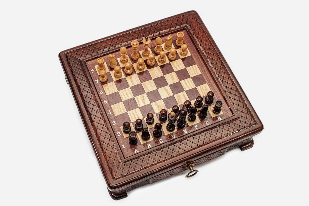 Top angle of the compact carved chess board with light and dark pieces arranged for play