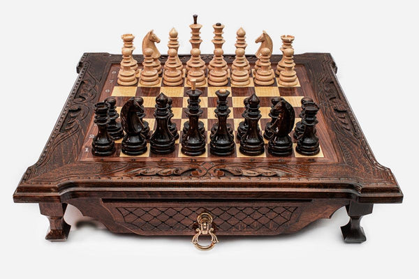 Dark walnut wooden chess set with scroll-carved corners and wooden pieces set up on the inlaid board