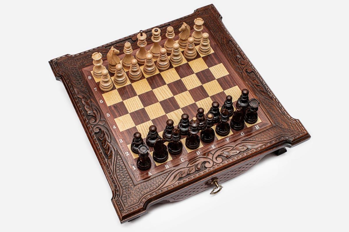 Top angle of the dark walnut chess board with carved scroll corners and pieces arranged for play