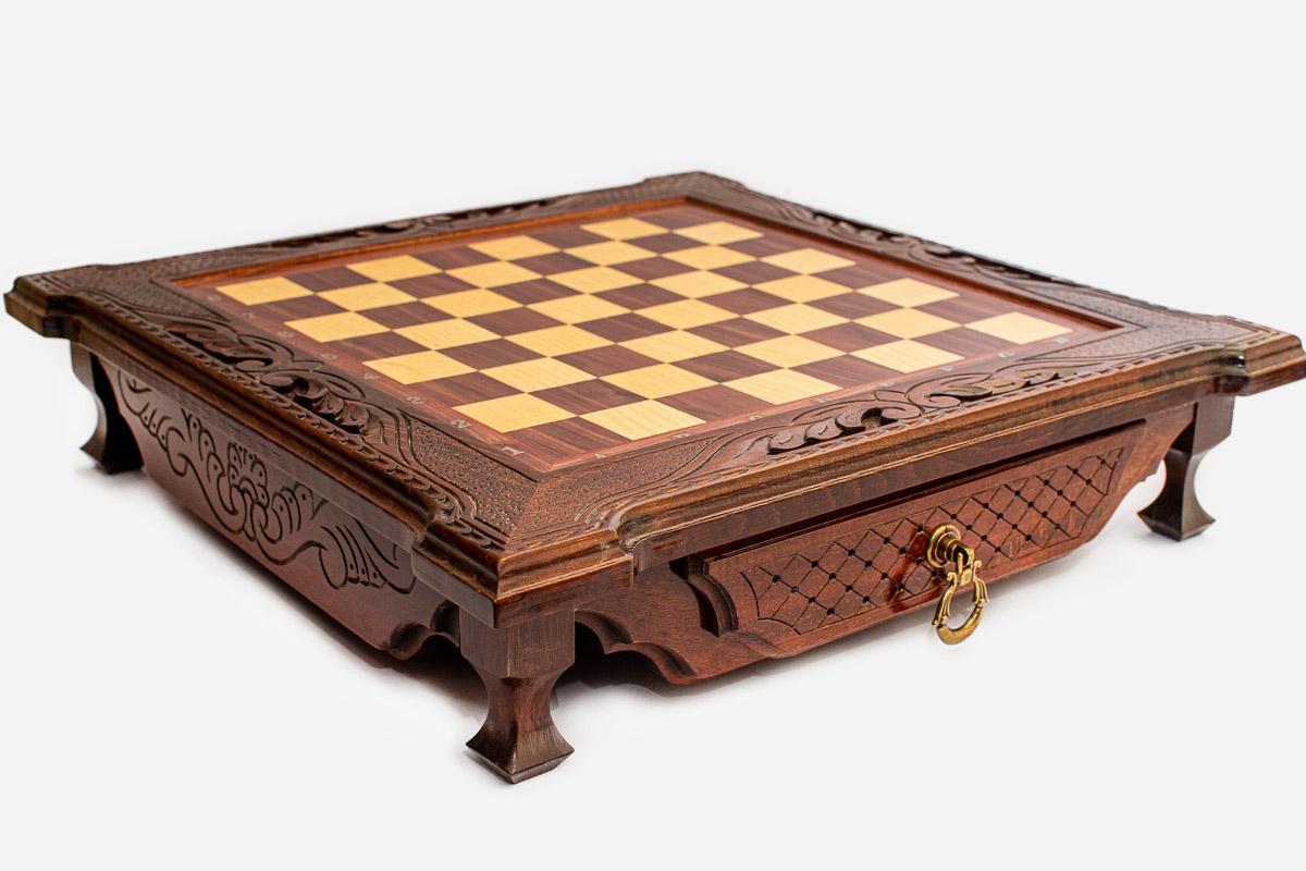 Angled view of the empty dark walnut chess board with carved corners and lattice-fronted drawer