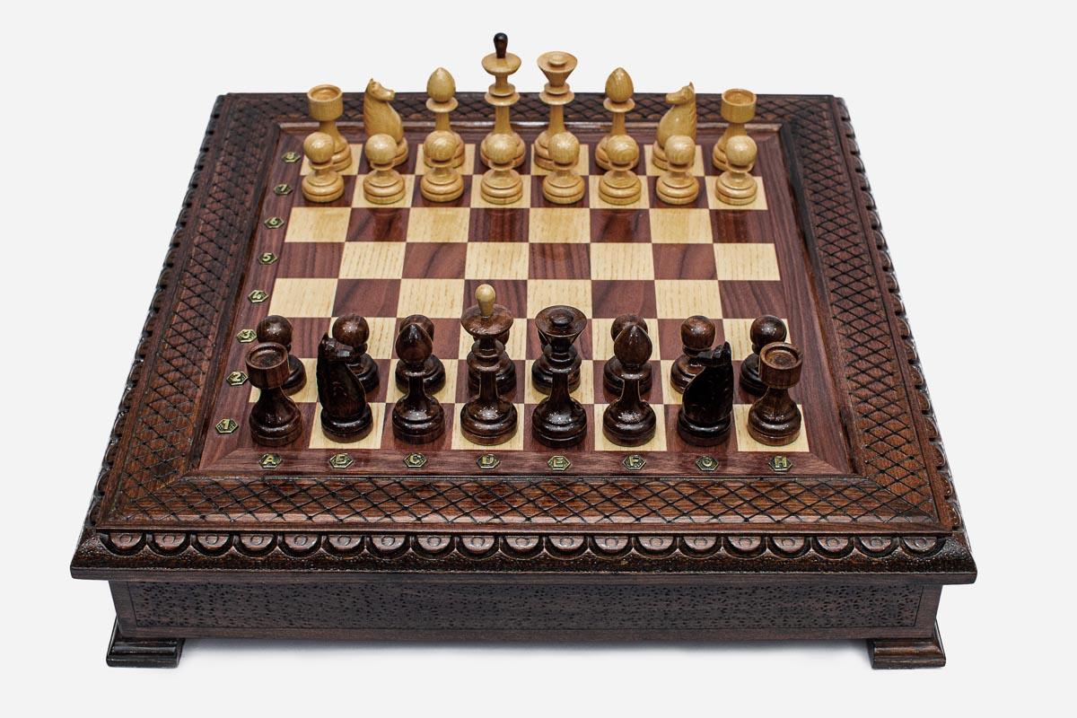 Wooden chess set in dark walnut finish with a carved lattice and beaded border and wooden pieces set up for play