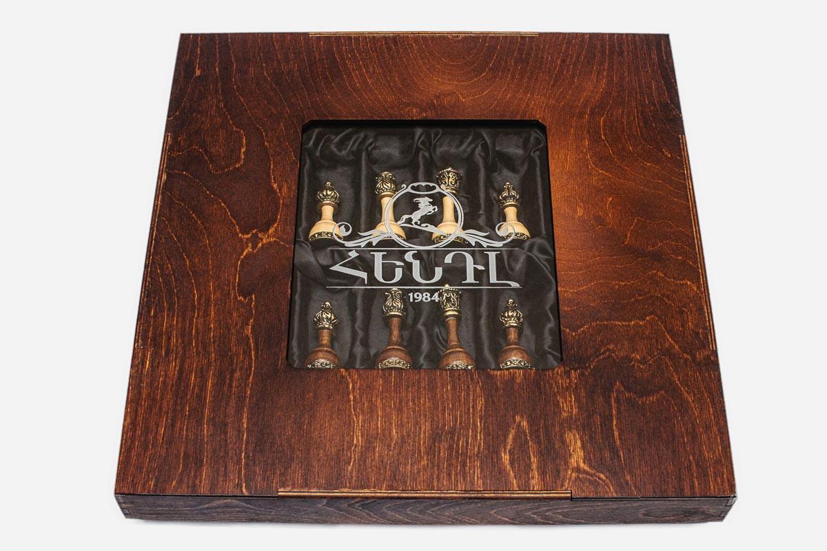 Gift box window revealing the brass-crowned king and queen chess pieces in satin