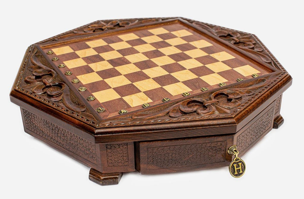 Angled view of the empty octagonal chess board with carved fleur-de-lis border and brass drawer pull