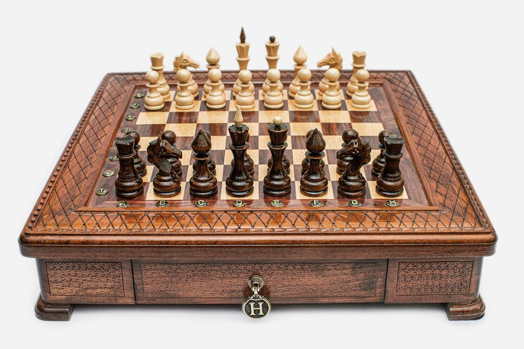 Square wooden chess set with carved diamond-lattice border and wooden pieces set up on the walnut and maple board