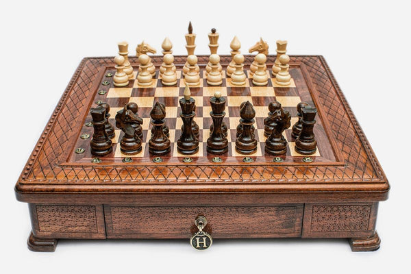 Square wooden chess set with carved diamond-lattice border and wooden pieces set up on the walnut and maple board