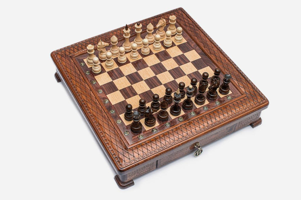 Angled top view of the square carved chess board with light and dark pieces arranged for play