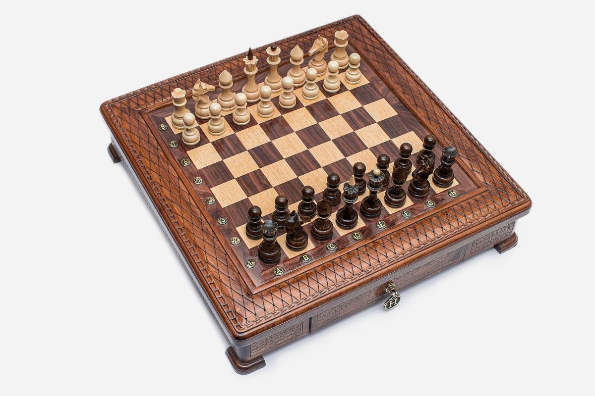 Angled top view of the square carved chess board with light and dark pieces arranged for play