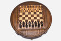 Round wooden chess set with woven lattice-carved border and wooden pieces set up on the inlaid board
