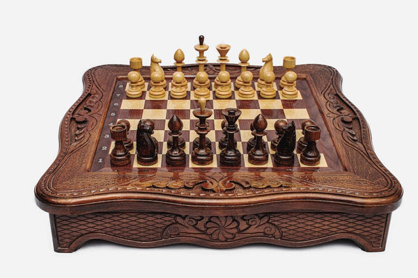 Handmade wooden chess set with carved scalloped frame and wooden pieces arranged on the walnut and maple board