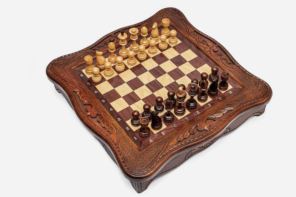 Angled top view of the carved chess board with light and dark wooden pieces set up for play
