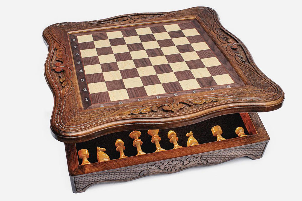 Storage drawer pulled out from the base of the chess set revealing the light wooden pieces inside